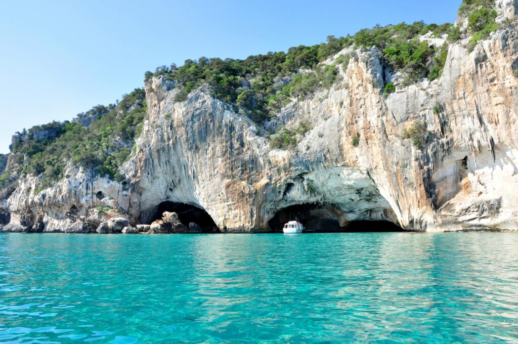 A boat enters a stunning cave along the rocky coastline of the Mediterranean Sea.