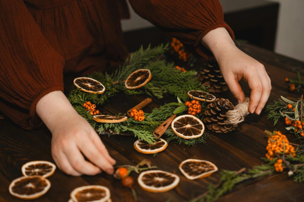 Hands arranging a DIY Christmas wreath with dried oranges.